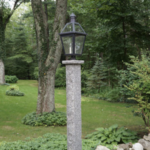 granite lamp post in a front yard surrounded by greenery and trees