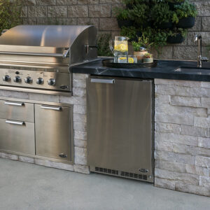 Outdoor kitchen with a grill, fridge, water pitcher and cabinets built with stone